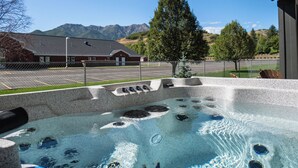 A hot tub with a mountain view, a fenced parking area, and a building in the background. - Powderline Lodge | Hot Tub | 2 King Suites | Ski (Mountain Green)