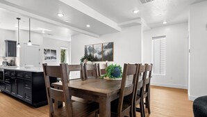 A modern kitchen with a dining area, featuring a wooden table and chairs, a black cabinet, and a window with a view. - Powderline Lodge | Hot Tub | 2 King Suites | Ski (Mountain Green)