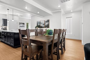 A modern kitchen with a dining area, featuring a wooden table and chairs, a black cabinet, and a window with a view. - Powderline Lodge | Hot Tub | 2 King Suites | Ski (Mountain Green)