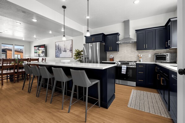 A modern kitchen with a large island, bar stools, stainless steel appliances, and dark cabinetry. - Powderline Lodge | Hot Tub | 2 King Suites | Ski (Mountain Green)