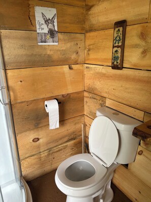 A wooden-paneled bathroom with a toilet, a roll of toilet paper, and a wall-mounted picture of a donkey. - Serenity Ridge. Enchanting 1-bedroom cabin in Wells perfect for a cozy getaway (Wells)