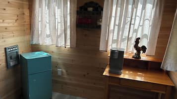 A room with wooden walls, a teal refrigerator, a coffee maker, and a rooster statue on a wooden table.