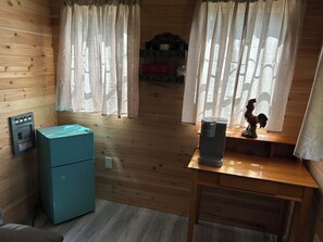 A room with wooden walls, a teal refrigerator, a coffee maker, and a rooster statue on a wooden table.