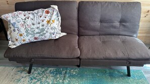 En brun soffa med ett blommigt prydnadskuddöverdrag, placerad framför en vägg av trä.