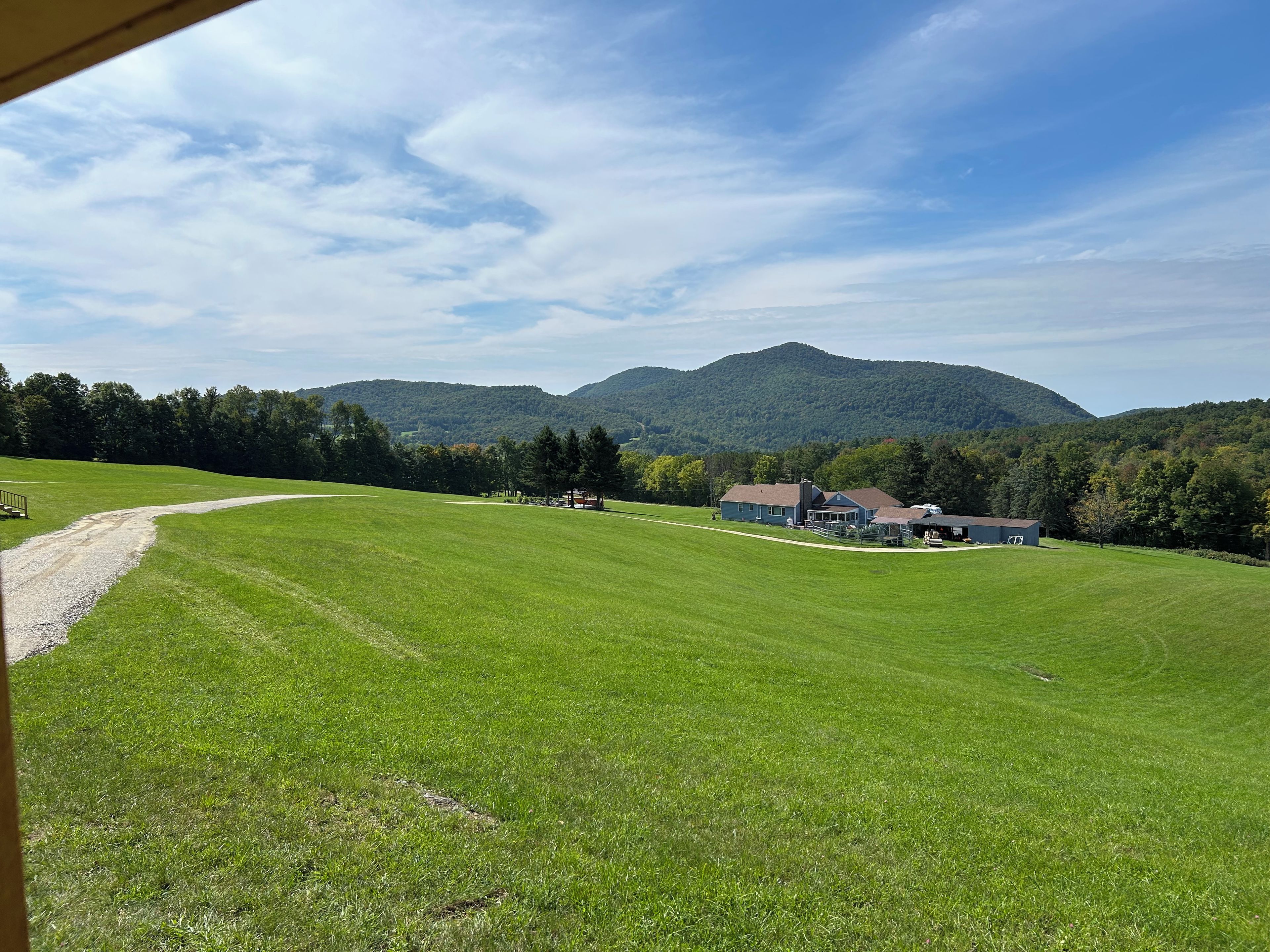 A rural landscape with a house, a gravel path, and a mountain in the background.
