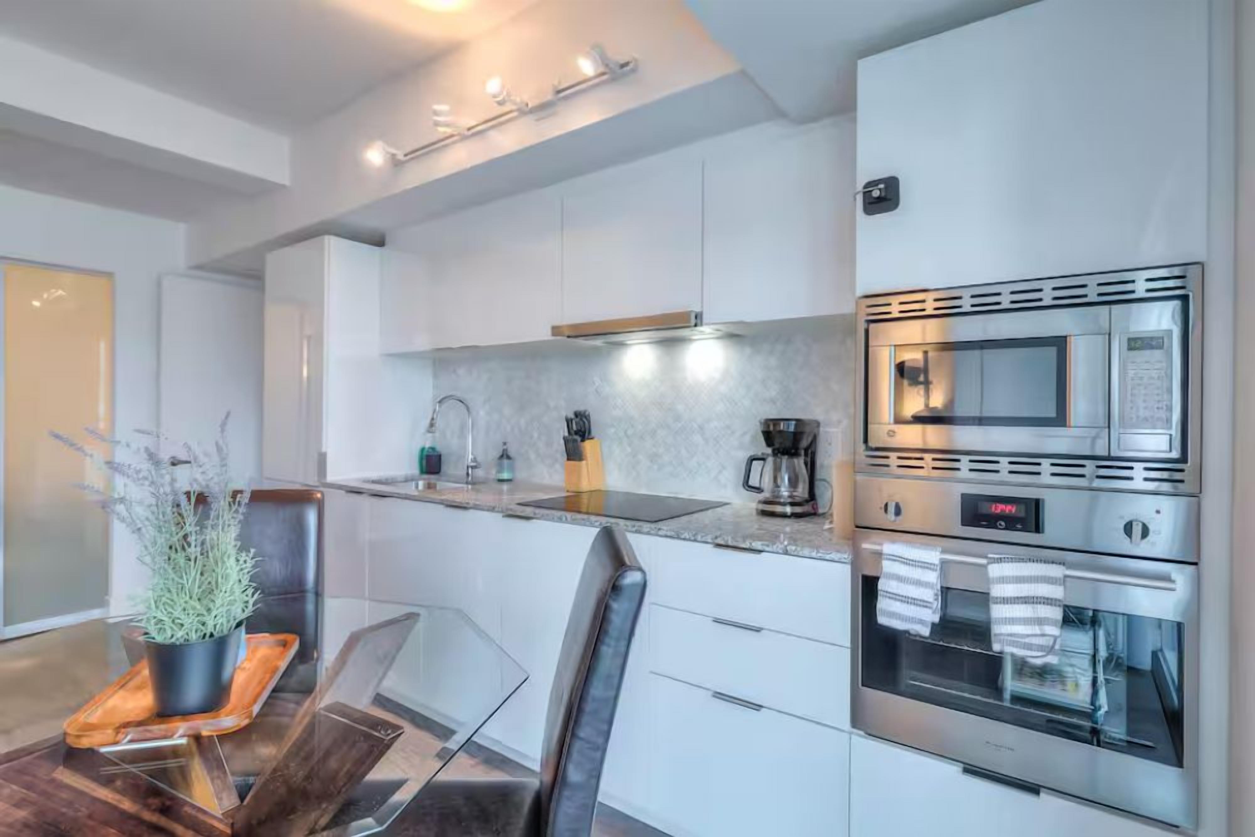 A modern kitchen with white cabinets, stainless steel appliances, and a glass dining table.