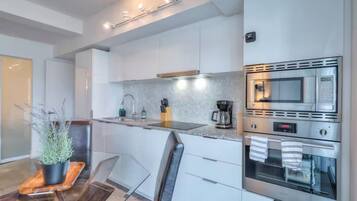 A modern kitchen with white cabinets, stainless steel appliances, and a glass dining table.