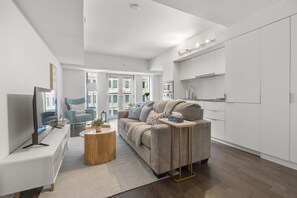 A modern living room with a sofa, coffee table, and TV. There is a kitchen area with cabinets and a countertop. - StayToronto - The Bay Residences (Toronto)