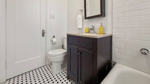 Une salle de bain comprenant des toilettes, un meuble en bois foncé, un lavabo blanc avec un plan en marbre et une baignoire.