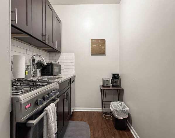 A compact kitchen with a gas stove, microwave, and a coffee maker on a small table.