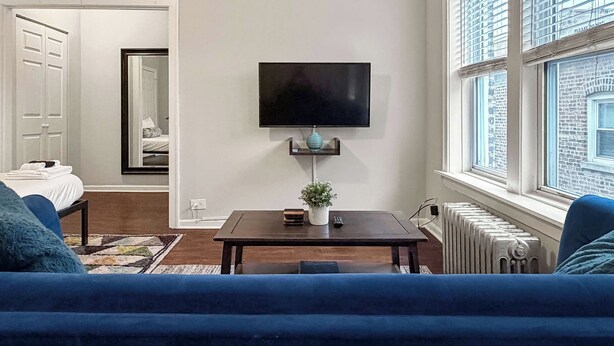 Un salon moderne avec un téléviseur à écran plat fixé au mur, une petite table sur laquelle est posée une plante en pot et un canapé bleu.