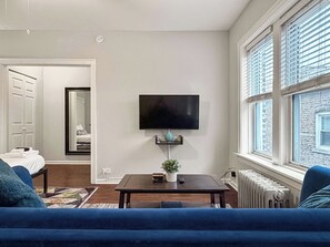 A modern living room with a flat-screen TV mounted on the wall, a small table with a potted plant, and a blue sofa.