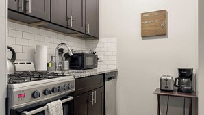 Une cuisine moderne avec des meubles de couleur sombre, une cuisinière à gaz, un four à micro-ondes, une machine à café et un petit espace évier.