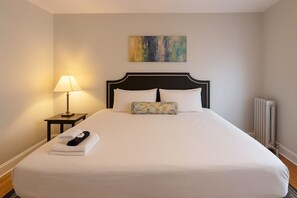 Een net opgemaakt bed met witte lakens, een zwart hoofdbord en een enkel kussen. Een lamp staat op een klein tafeltje naast het bed, en er ligt een handdoek opgevouwen op het bed.