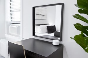A modern hotel room with a large mirror, a bedside table with a white object, and a window with blinds. - Ideal 1-Bedroom Stay (Chicago)