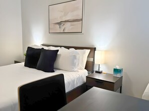 A hotel room with a neatly made bed, a bedside table with a lamp, and a framed abstract painting on the wall. - Ideal 1-Bedroom Stay (Chicago)
