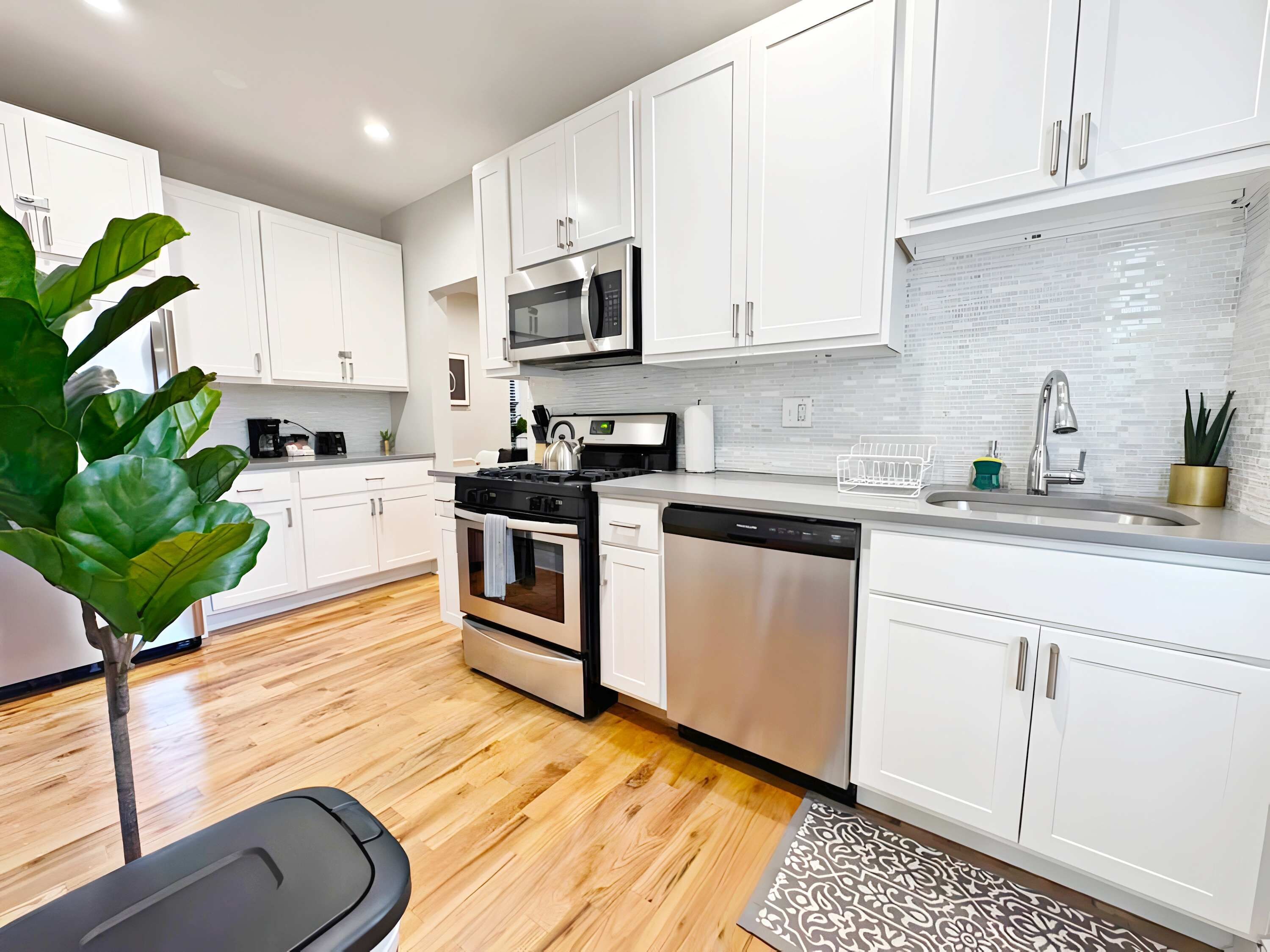 A modern kitchen with white cabinets, stainless steel appliances, and a wooden floor.