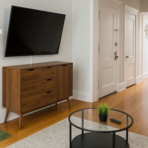A modern living room with a flat-screen TV, wooden cabinet, and a glass coffee table with a plant. - Boystown Chic 2BR Escape (Chicago)