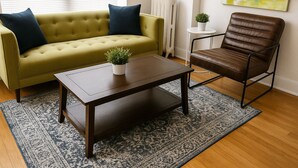 A living room with a sofa, a coffee table, a chair, a radiator, and a painting on the wall. - 1BR Fully Equipped & Central (Chicago)