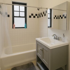 Een badkamer met een bad, een wastafel, een spiegel en een raam met gordijn.