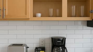 Une cuisine équipée d’un grille-pain, d’une machine à café et d’une étagère où sont rangées des tasses et des verres.