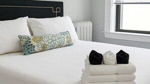 A neatly made bed with a white duvet, a decorative pillow, and a stack of folded towels. - 1BR Fully Equipped & Central (Chicago)