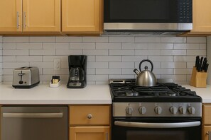 A kitchen with a toaster, coffee maker, kettle, stove, oven, and wooden cabinets. - 1BR Fully Equipped & Central (Chicago)