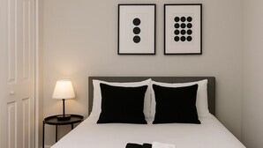 Cama bem arrumada com roupa de cama preta e branca, um cobertor preto e duas obras de arte abstrata emolduradas na parede.