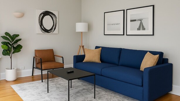 Uma sala de estar moderna com um sofá azul, uma poltrona marrom, uma pequena mesa de centro preta, um abajur e um vaso com planta.