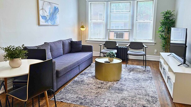 A modern living room with a grey sofa, two armchairs, a coffee table, and a TV. - Chic & Fully Furnished 2BR Apartment (Chicago)
