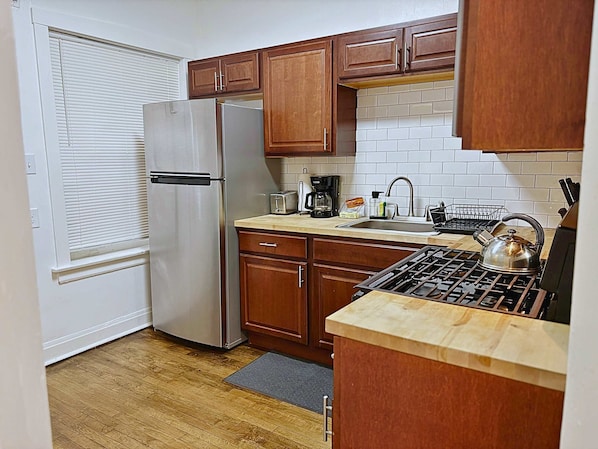 A compact kitchen with wooden cabinets, a stainless steel refrigerator, a sink, and a stove.
