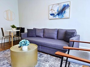 A modern living room with a grey sofa, a round gold side table, and a blue vase.