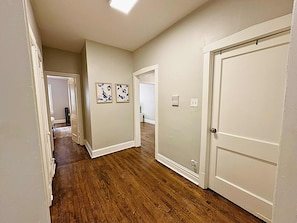 A hallway with wooden flooring, white walls, and two doors. There are two framed pictures on the wall.