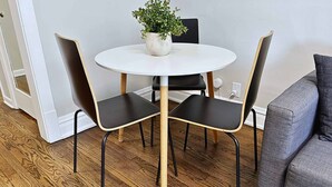 A dining area with a round white table, two black chairs with wooden legs, and a potted plant on the table. - Chic & Fully Furnished 2BR Apartment (Chicago)