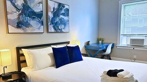 A hotel room with a bed, a desk, and two paintings on the wall. - Chic & Fully Furnished 2BR Apartment (Chicago)