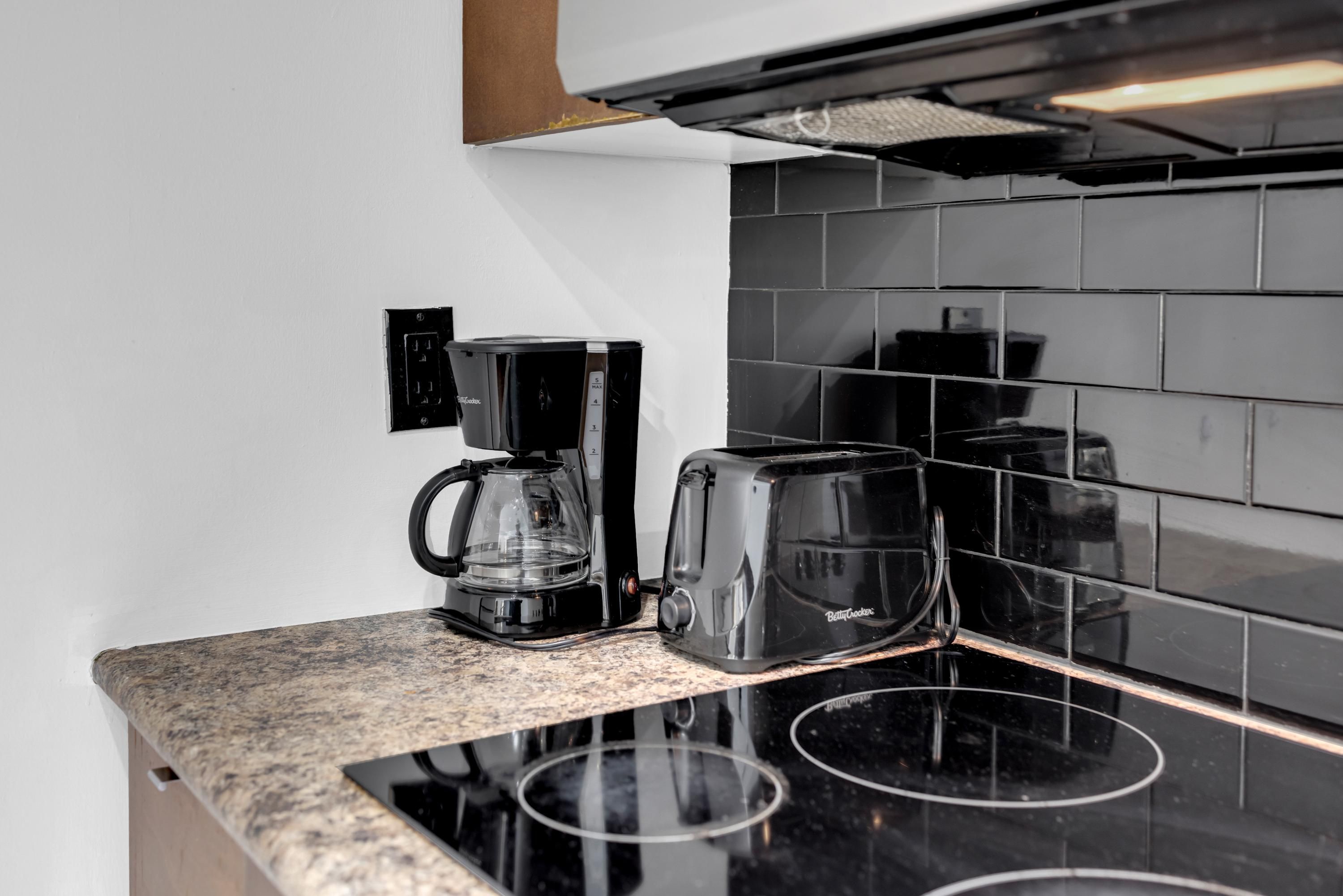 A kitchen with a black coffee maker, toaster, and black-tiled backsplash.