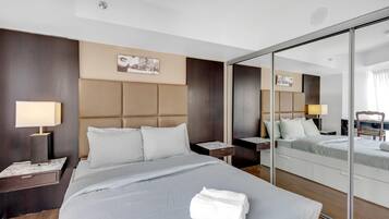 A hotel room with a large bed, a bedside table with a lamp, a mirror, and a wooden floor.