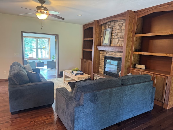 A living room with a fireplace, wooden shelving, and a ceiling fan.