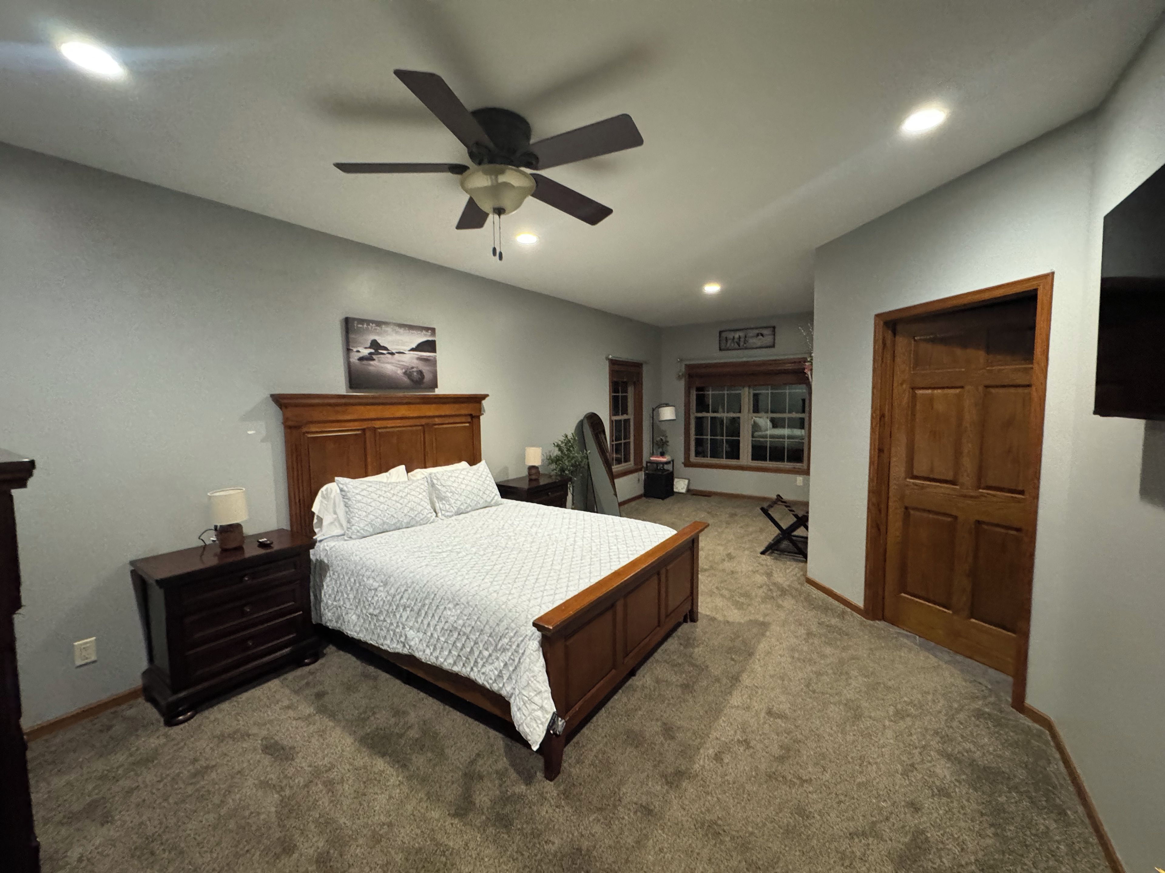 Ein Schlafzimmer mit Bett, Deckenventilator, Nachttisch, Lampe, Fenster und Tür.