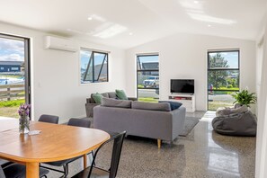 A modern living room with a grey sofa, a TV, and a dining area with a wooden table.