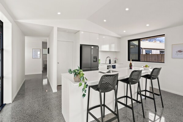 A modern kitchen with a central island, bar stools, and a view of the outside.