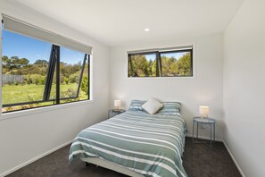 A bedroom with a large window, a bed with striped bedding, two bedside tables with lamps, and a view of greenery outside.