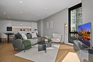 A modern living room with a sofa, coffee table, and a TV displaying a cityscape. - Skyline 3-Bed Apartment Near South Melbourne (South Melbourne)