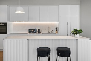 A modern kitchen with white cabinetry, a built-in microwave, a coffee machine, and a potted plant. - Skyline 3-Bed Apartment Near South Melbourne (South Melbourne)