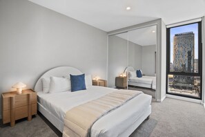 Ein modernes Schlafzimmer mit einem großen Bett, Nachttischen, einem Spiegel und Blick auf die Stadt.