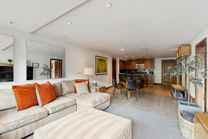Een moderne woonkamer met een modulaire bank, een eethoek met een glazen tafel en een keuken met houten kasten.