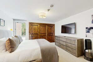 Ein Schlafzimmer mit Bett, Holzschrank, einem an der Wand montierten Fernseher und einer Kaffeemaschine.