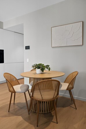 A dining area with a round table, two wicker chairs, a potted plant, and a wall-mounted artwork. - Panoramic 2-Bed Apartment Near South Melbourne (South Melbourne)