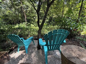 Two green Adirondack chairs facing each other with a tree in the background.