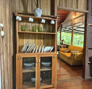 A wooden cabinet with glassware and plates, a yellow sofa, and a view of greenery. - Costa Rican Country Style house in adorable Sámara Beach with cool AC breeze (Sámara)